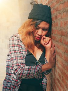 young woman leans against a brick wall feeling upset
