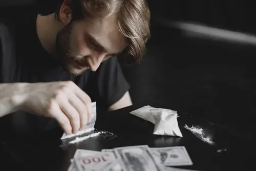 man using cocaine on a table with money on it