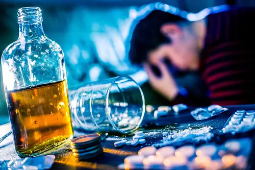 man looking down with alcohol and pills on table